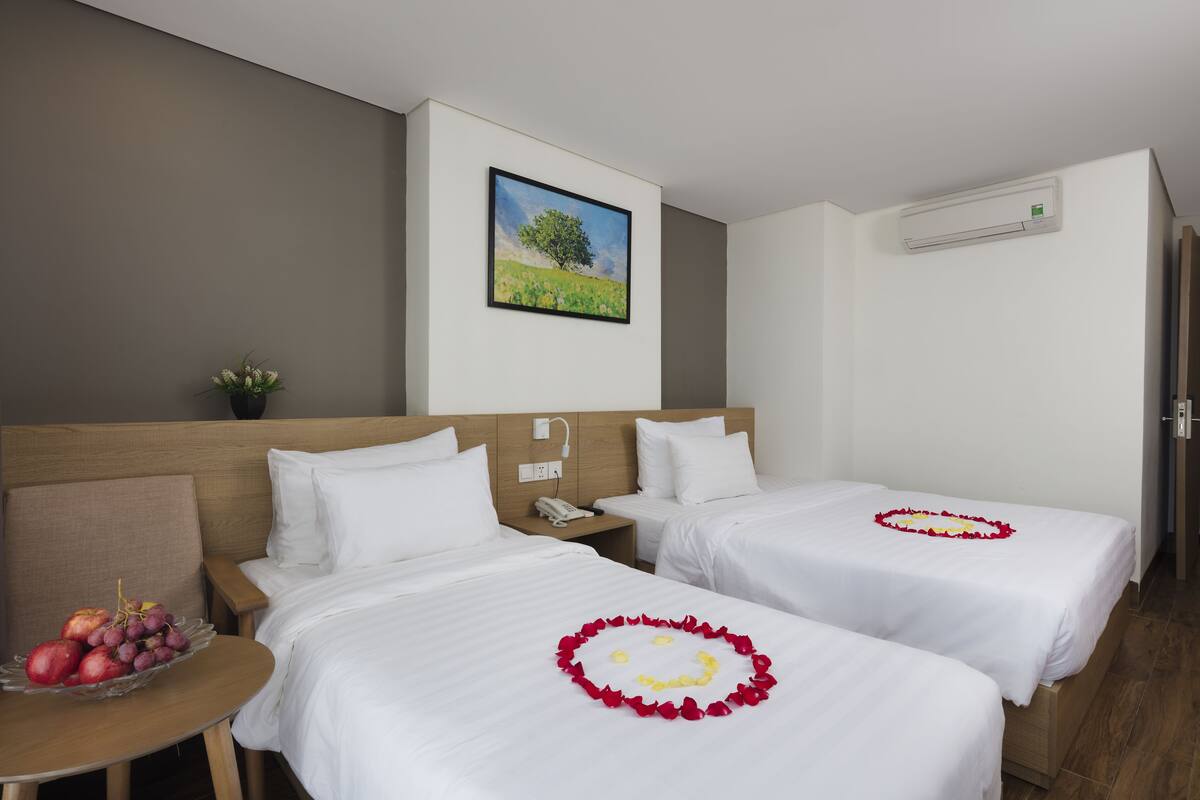 A hotel room with two beds, a small table with fruit, and a painting on the wall.