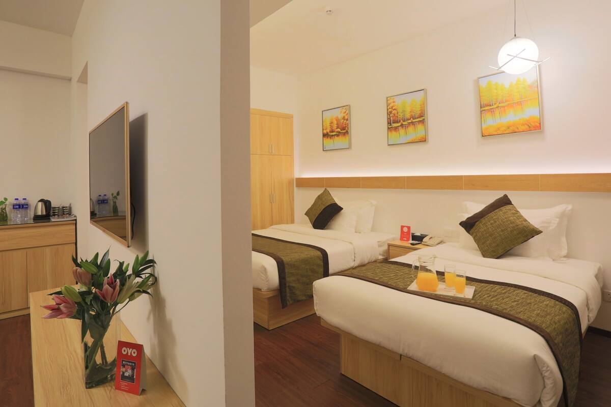 A hotel room with two beds, a wooden headboard, a flat-screen TV, and artwork on the wall.