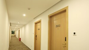 Un couloir d’hôtel avec des portes en bois, un revêtement de sol en moquette et un éclairage encastré.