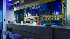 Un espace bar avec des étagères en bois remplies de différentes bouteilles, un comptoir avec une caisse enregistreuse et des verres à vin suspendus.