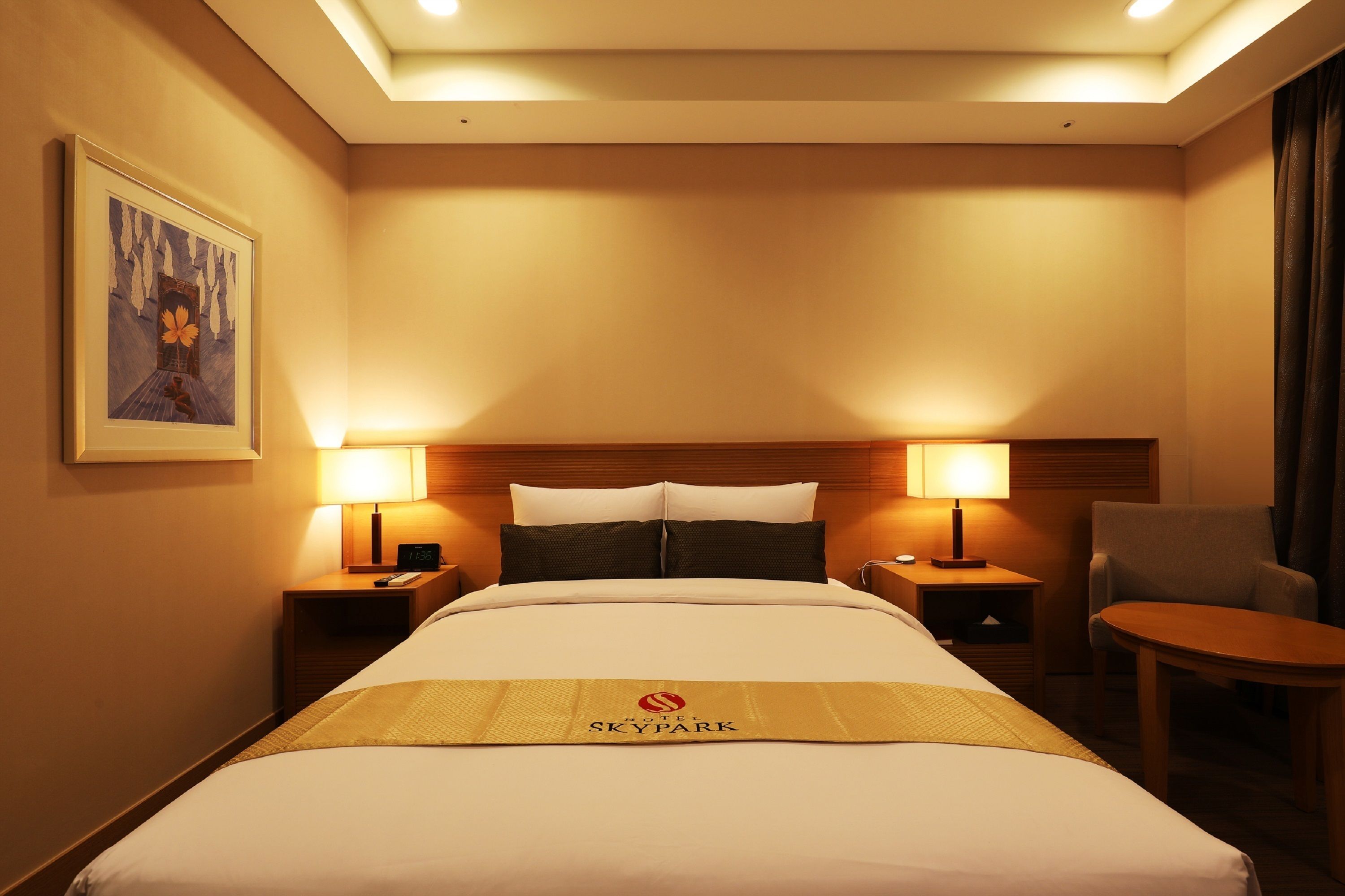 Ein Hotelzimmer mit einem großen Bett, zwei Nachttischen mit Lampen, einem Sessel und einem gerahmten Bild an der Wand.
