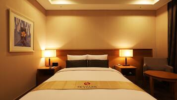 Ein Hotelzimmer mit einem großen Bett, zwei Nachttischen mit Lampen, einem Sessel und einem gerahmten Bild an der Wand.