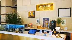 Un espace d’accueil avec une enseigne indiquant « Le Blanc Coffee & Dessert », un distributeur d’eau, des œuvres d’art encadrées et une vitrine en verre contenant des bouteilles.
