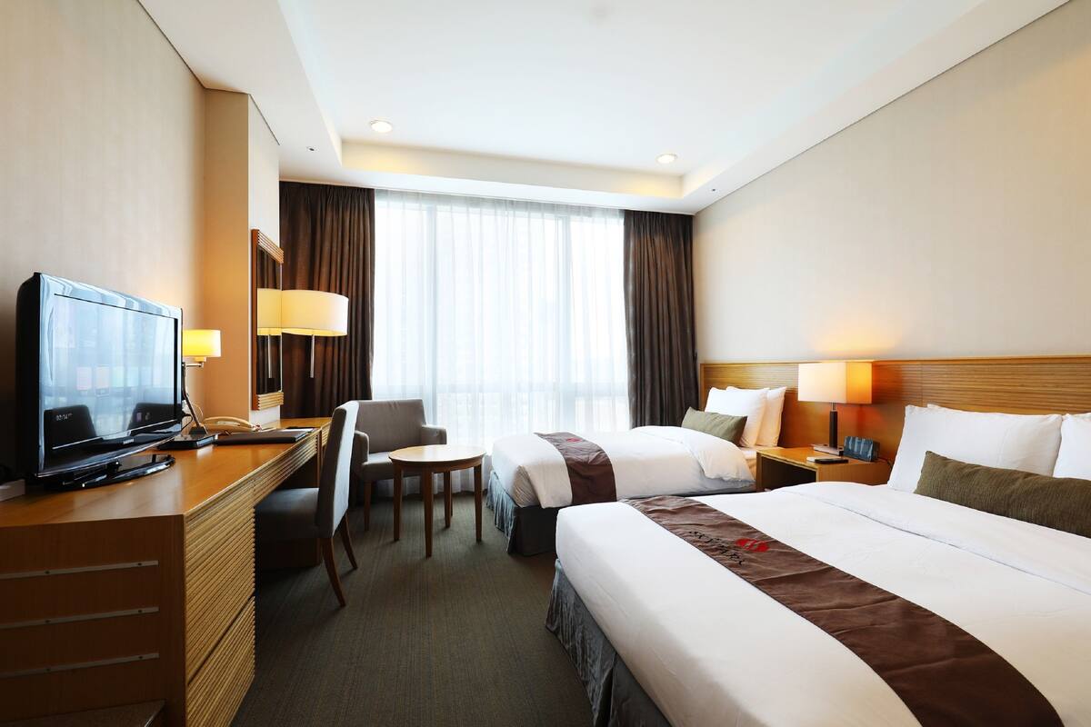 A hotel room with a desk, two beds, a TV, and a window with curtains.