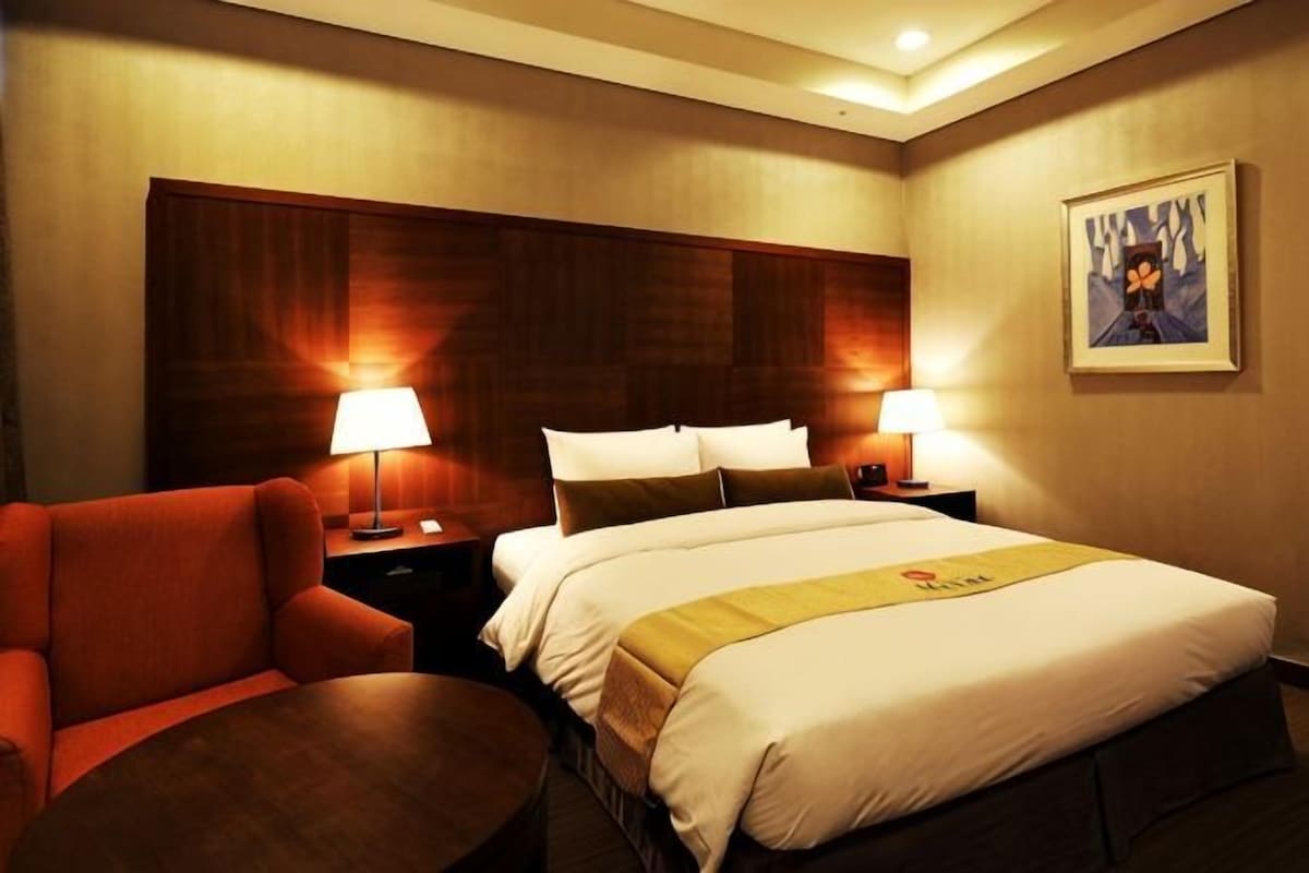 Una habitación de hotel con una cama, dos mesitas de noche, una silla y una pequeña mesa.
