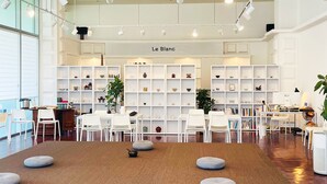 Un interior moderno con muebles blancos, una zona de estar central con cojines y estanterías con diversos objetos.