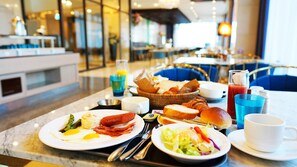 Un buffet de petit-déjeuner proposant une variété d’aliments, notamment des œufs, des saucisses et des viennoiseries, ainsi que des boissons et des condiments.