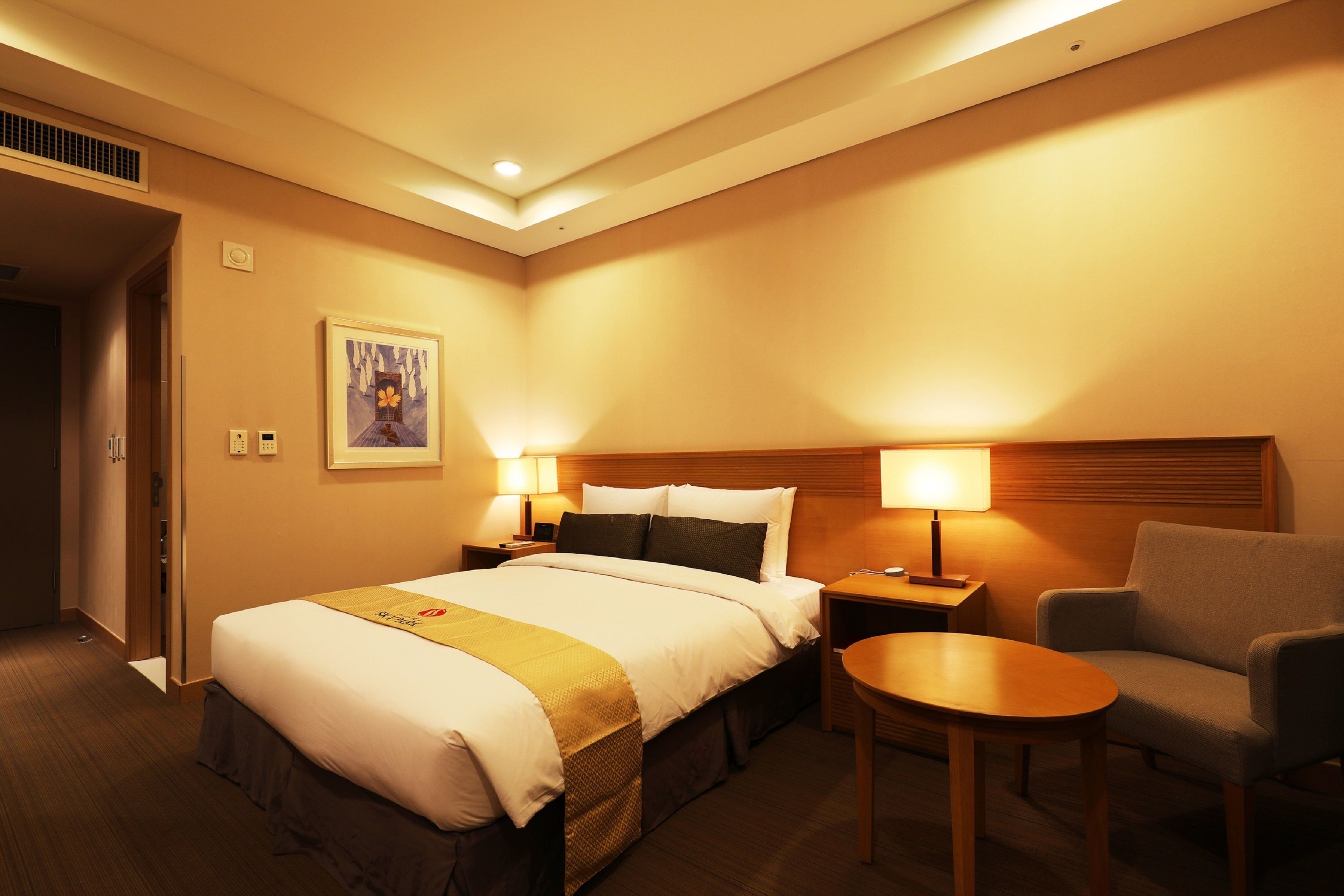 A hotel room with a large bed, two bedside tables with lamps, a chair, and a small table.