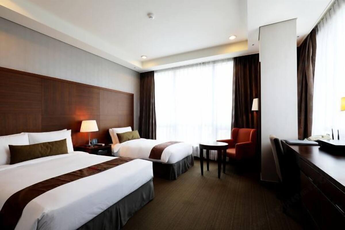 Une chambre d’hôtel avec deux lits, un bureau, une chaise et une petite table.