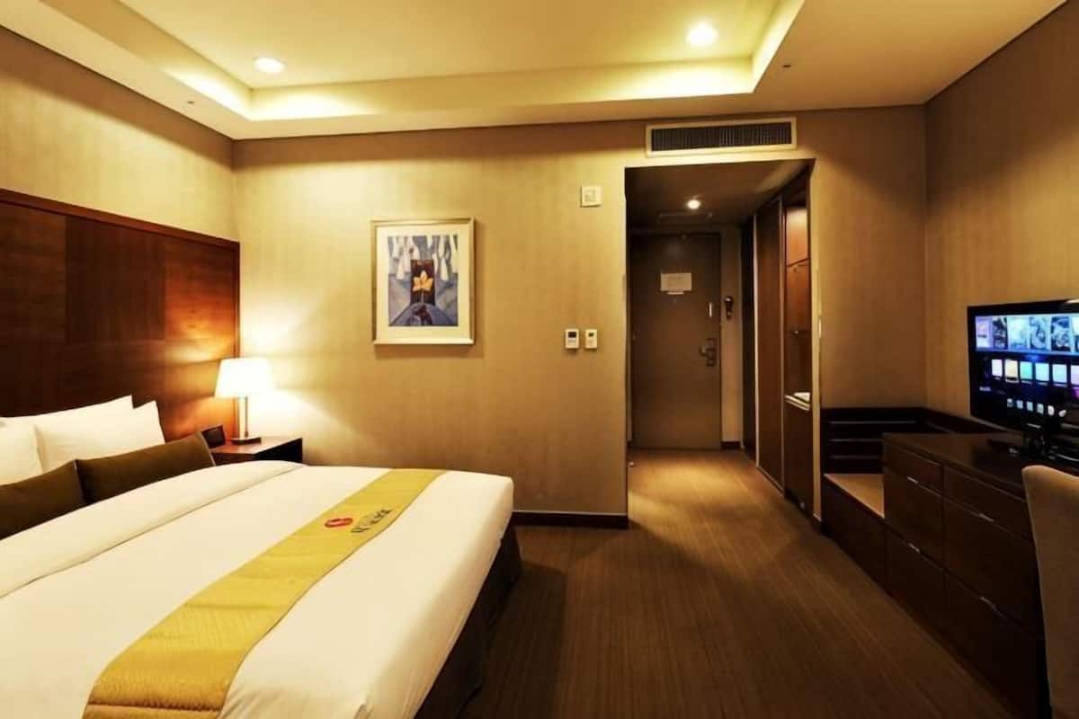 A hotel room with a bed, a desk, a television, and a door leading to a hallway.