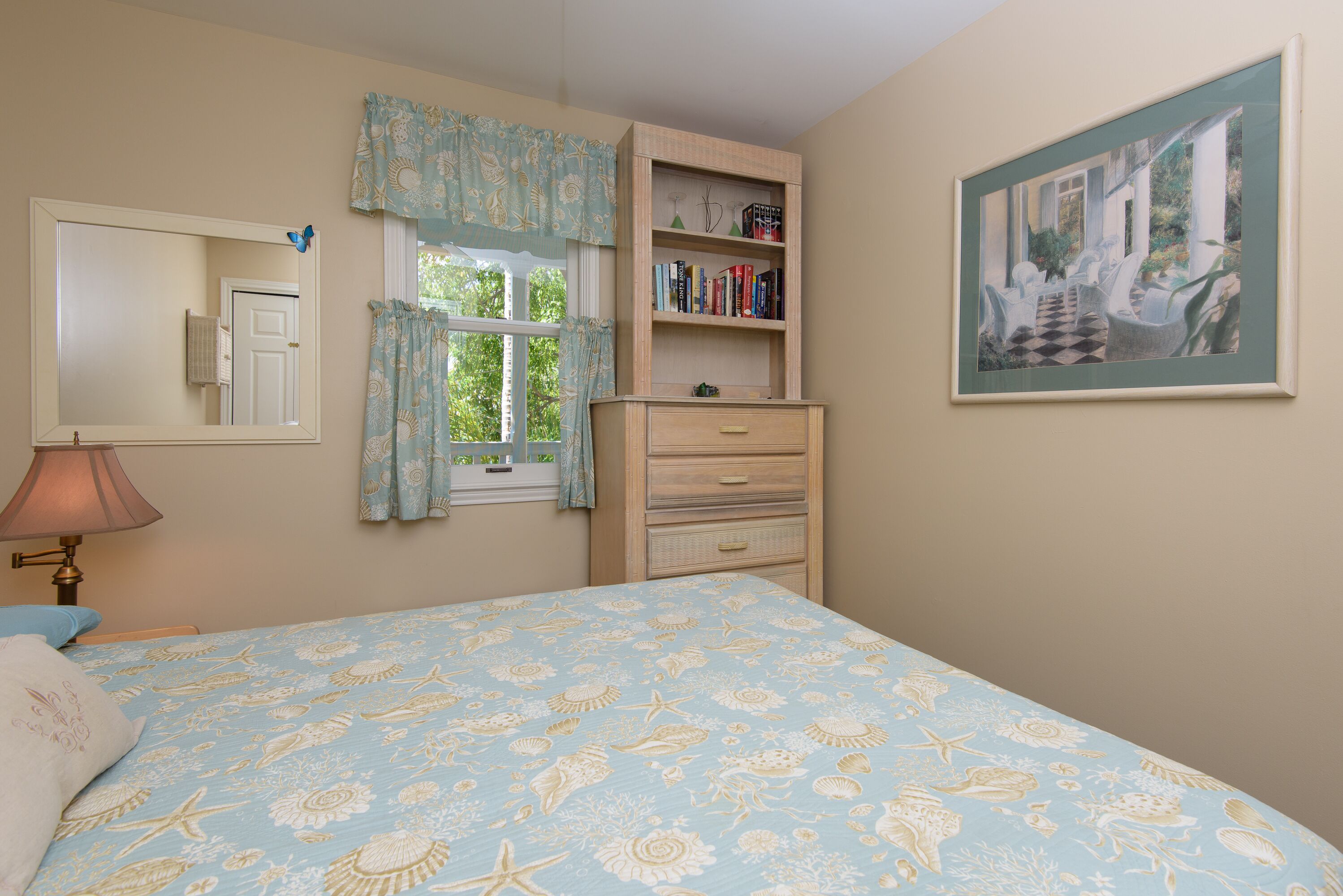 A bedroom with a bed, a dresser, a bookshelf, a window with curtains, a mirror, and a painting on the wall.