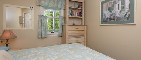 A bedroom with a bed, a dresser, a bookshelf, a window with curtains, a mirror, and a painting on the wall.