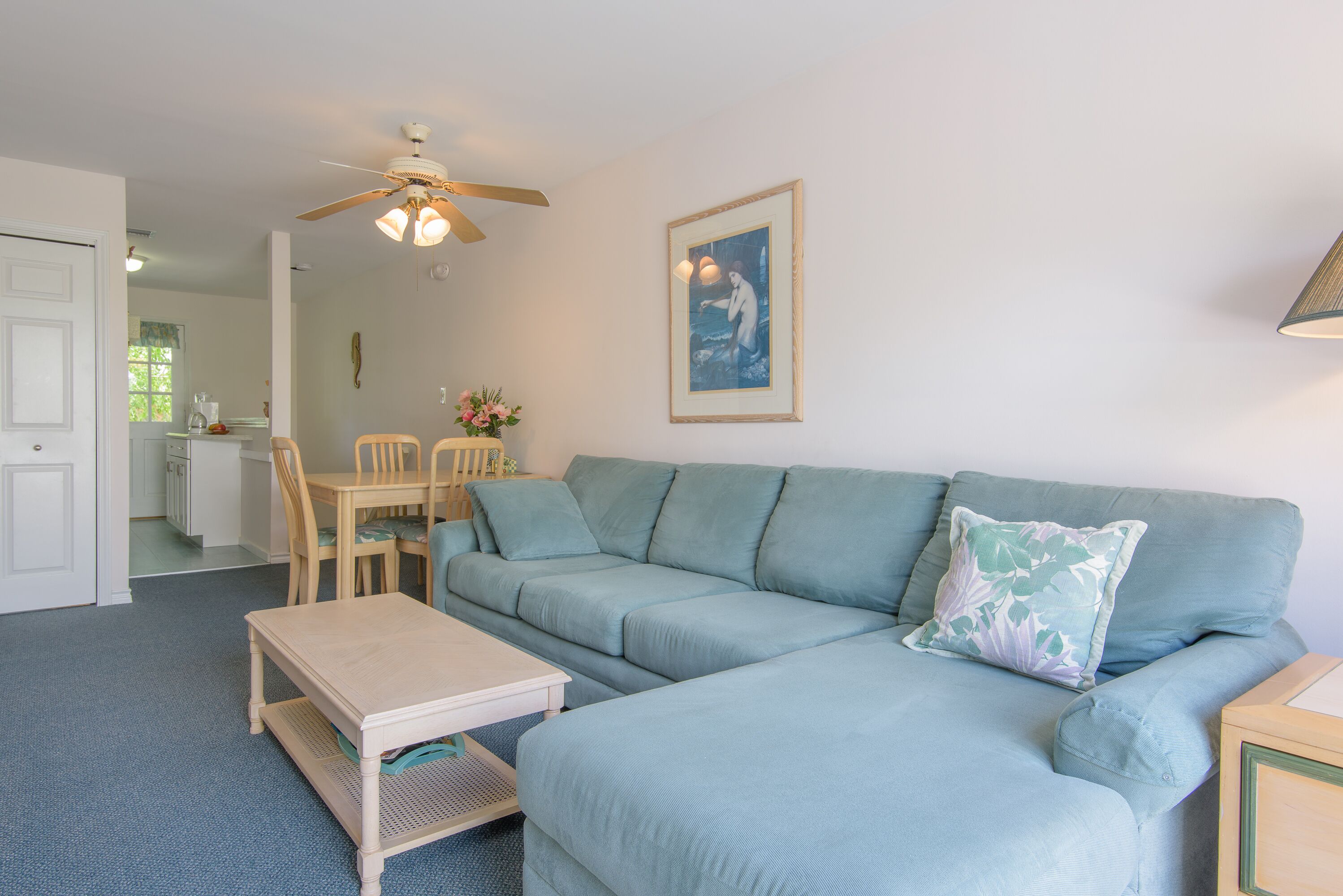 Ein Wohnzimmer mit einem hellblauen Sofa, einem Holztisch und einem Deckenventilator.