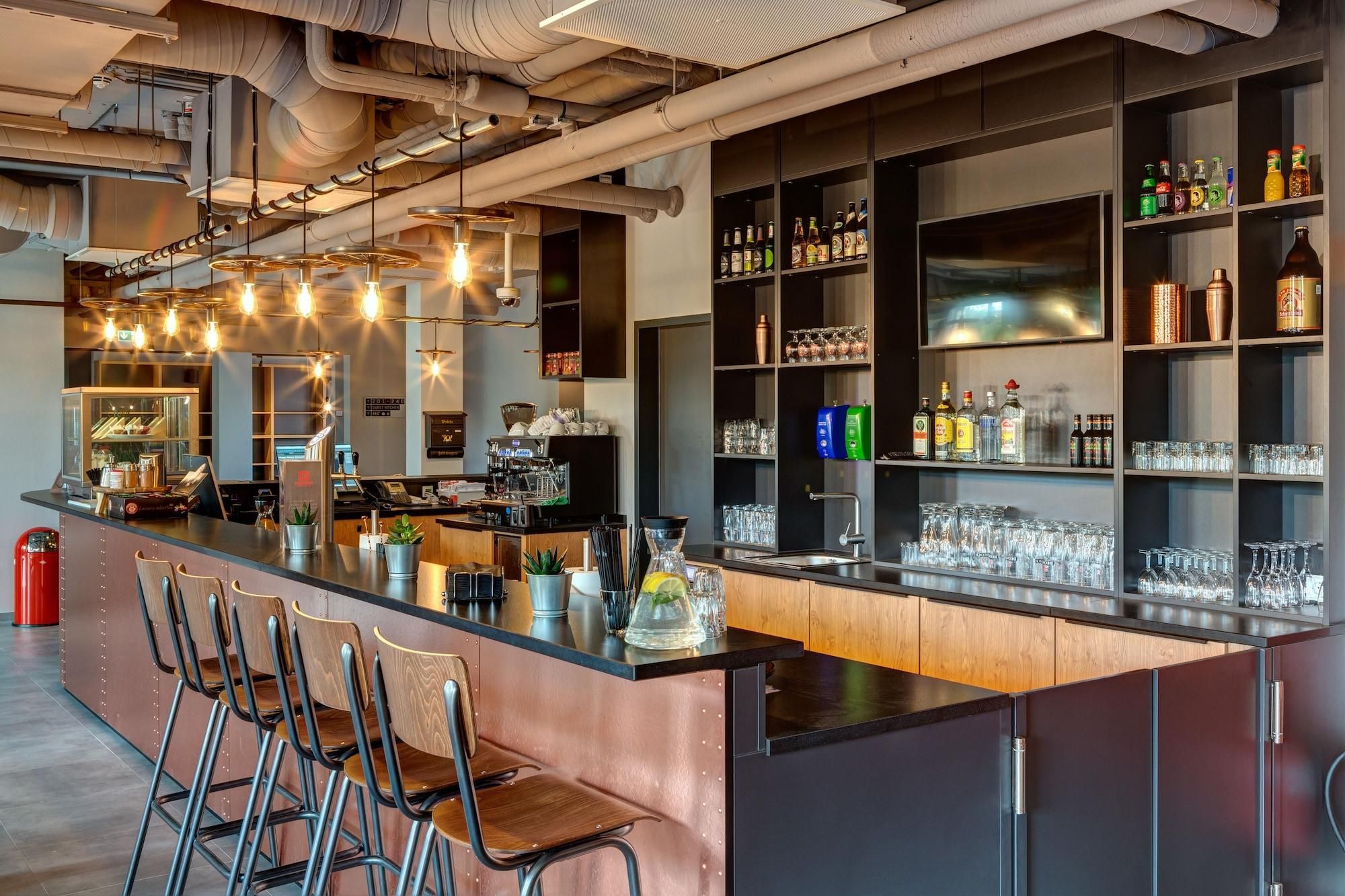 A bar area with a long counter, multiple seating options, and a variety of bottles and glasses on shelves.