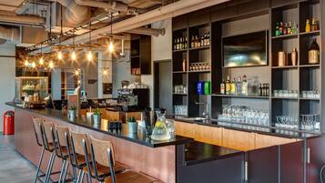 A bar area with a long counter, multiple seating options, and a variety of bottles and glasses on shelves.