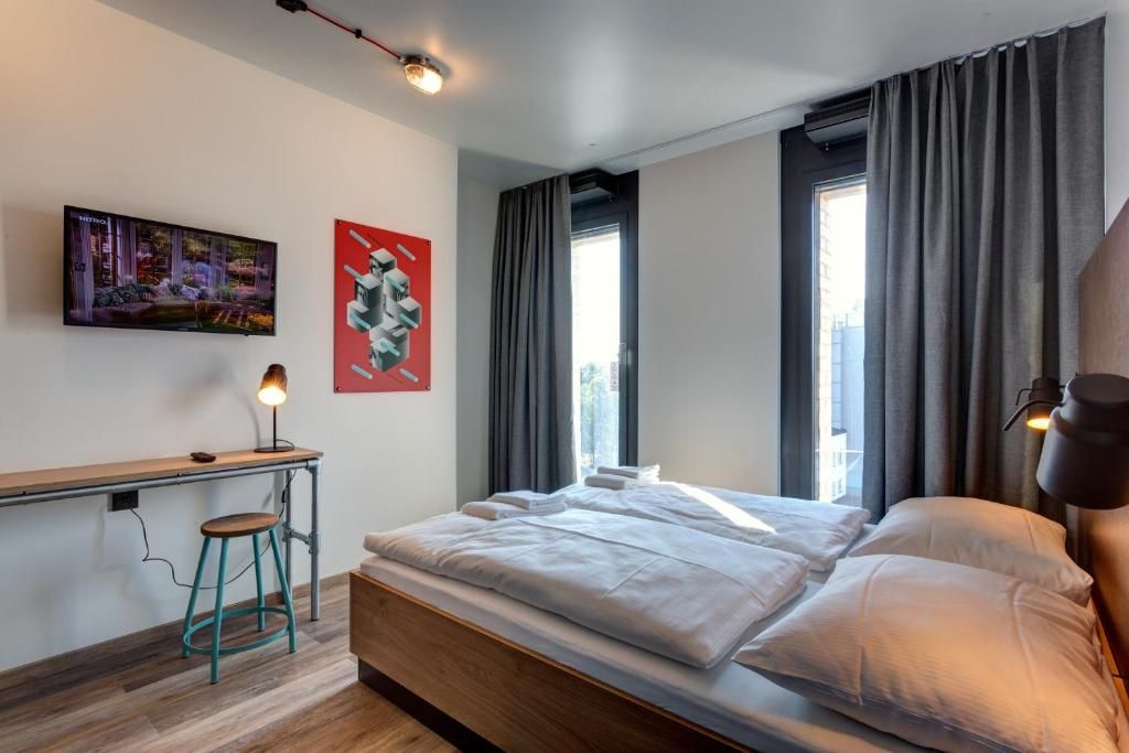 Una camera da letto moderna con un letto, una scrivania e una sedia. Al muro, un quadro e una finestra con tende.