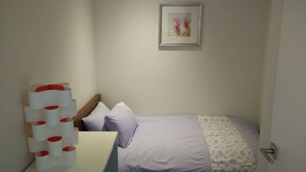 Un dormitorio con cama, almohadas, un estante en la pared y un cuadro enmarcado.