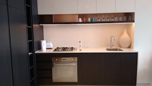 A modern kitchen with a stainless steel range, oven, and dishwasher, a white countertop, and a shelf with glassware. - Camberwell Holiday Apartment (Camberwell)
