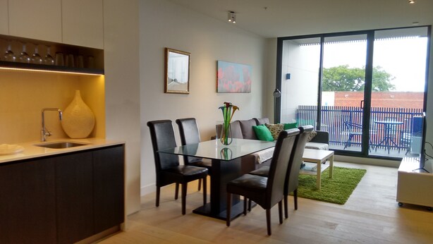 A modern kitchen with a dining area, a large window with a view of the outside, and a small balcony. - Camberwell Holiday Apartment (Camberwell)