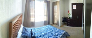 Une chambre à coucher avec un lit, une armoire, un bureau et une fenêtre avec des rideaux.