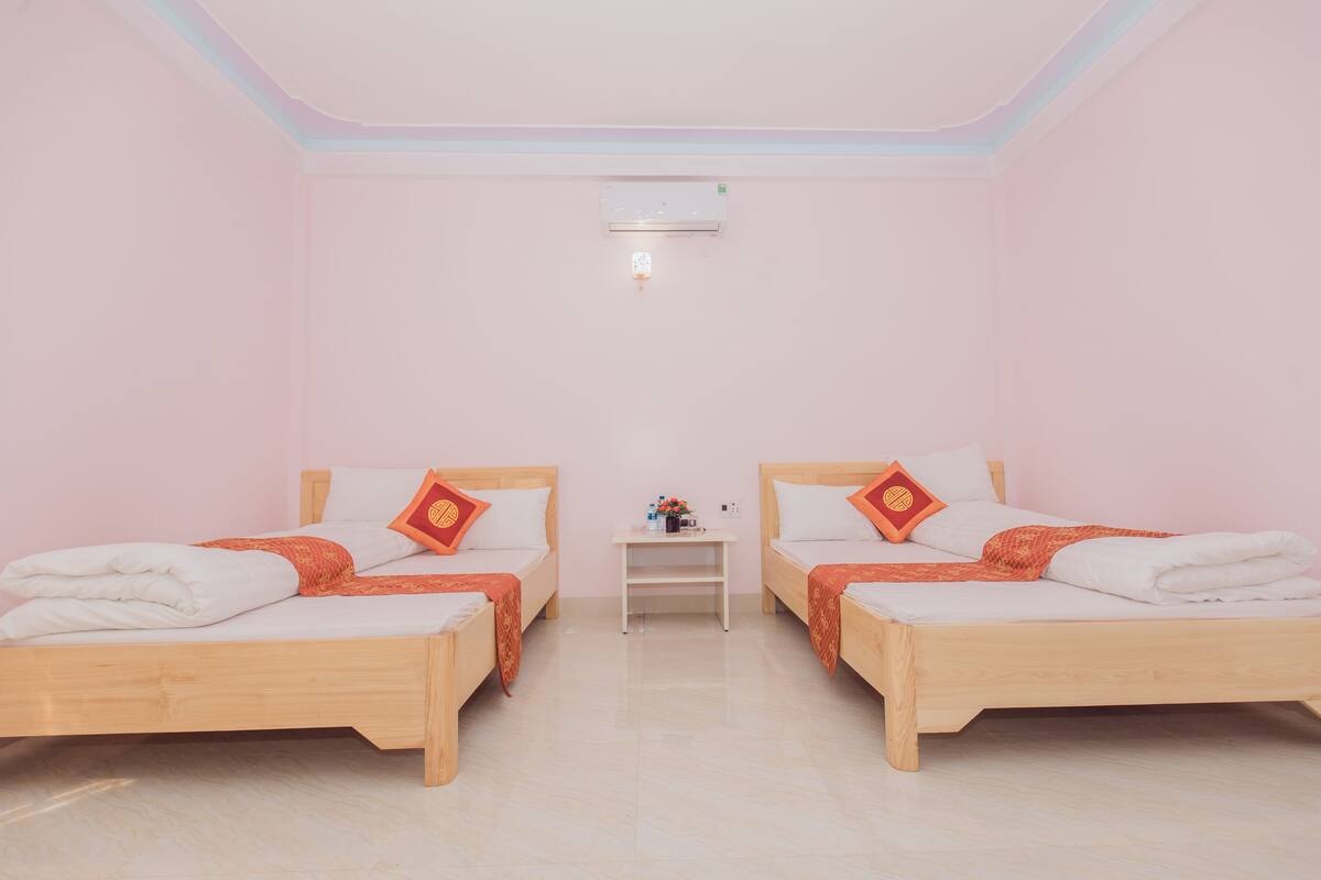 A room with two wooden beds, a small white nightstand, and an air conditioning unit on the ceiling.