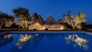 A house with a swimming pool, surrounded by trees and lit up at dusk.