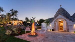 A stone building with a conical roof, a fire pit in the center, and outdoor seating.