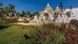 A traditional stone building with a conical roof, surrounded by a well-maintained garden with various plants and flowers.