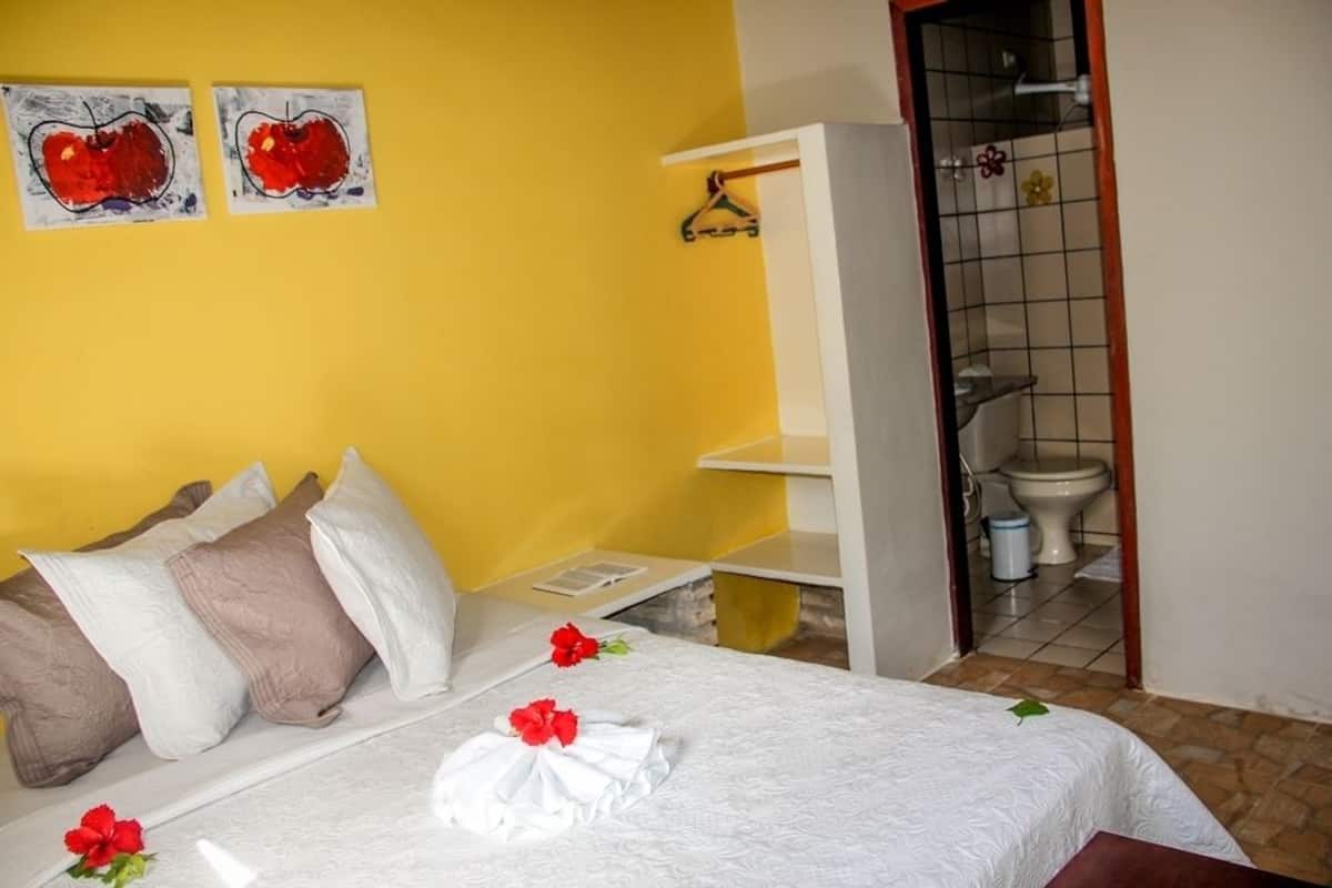 A hotel room with a bed, pillows, a towel, and a small bathroom visible through an open door.
