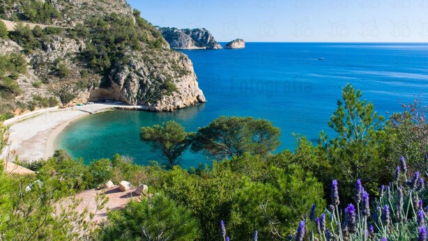 Paesaggio costiero con spiaggia, scogliere rocciose e mare cristallino blu.