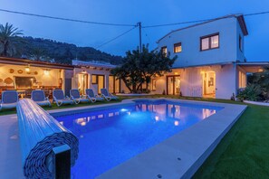 Une piscine avec des chaises longues, un bâtiment doté d’un toit plat et un arbre en arrière-plan.