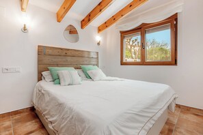Une chambre à coucher avec une tête de lit en bois, une grande fenêtre et un lit recouvert de linge de lit blanc.