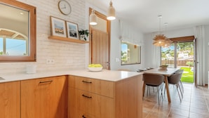 Una cucina moderna con mobili in legno, un piano di lavoro bianco e una zona pranzo con tavolo e sedie.