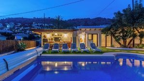 Una piscina con lettini, una zona relax all'ombra e vista su una comunità collinare.