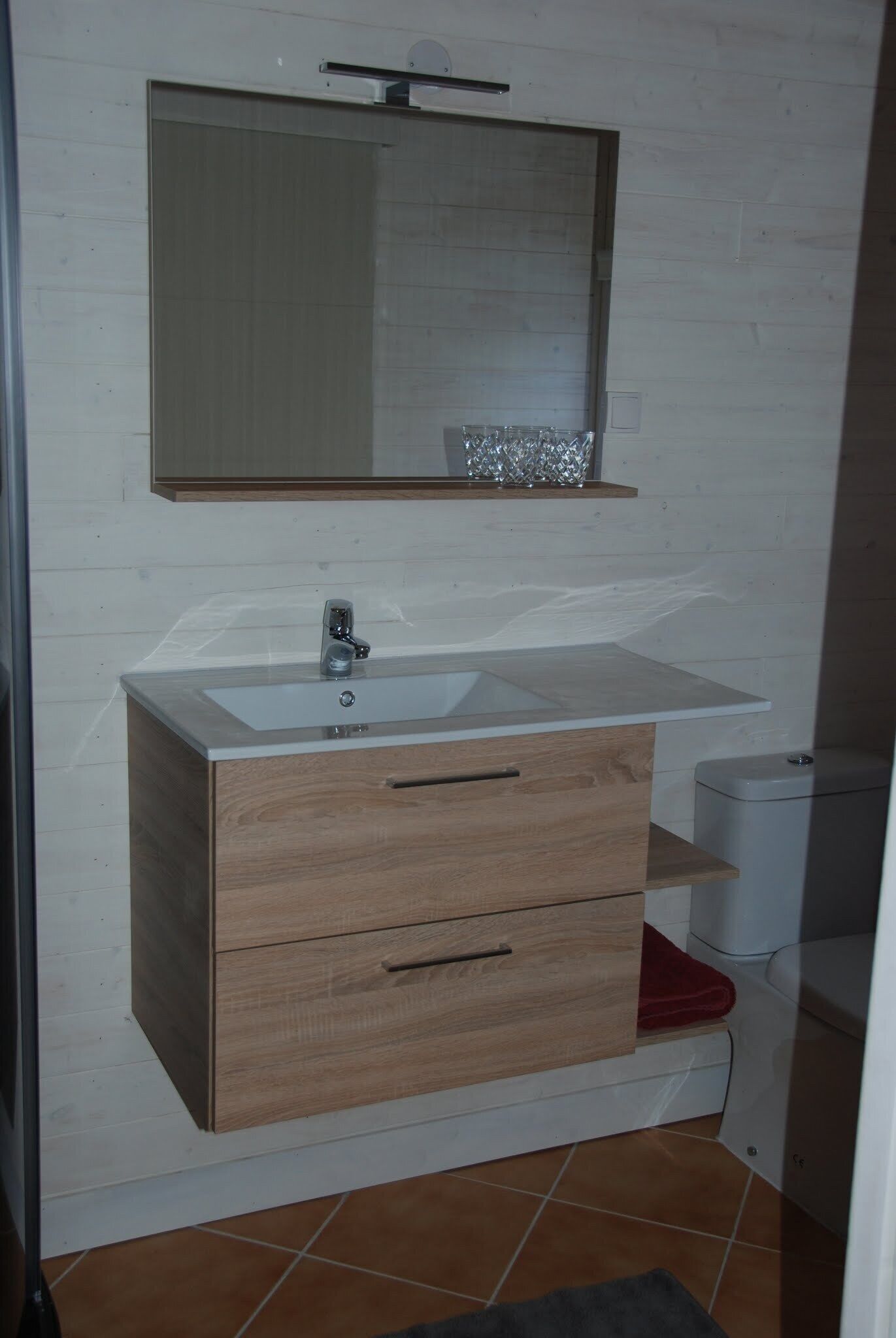 Un baño con lavamanos blanco, mueble de madera y un espejo encima.