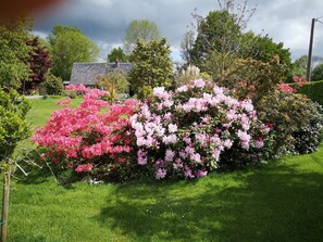 A garden with blooming pink and white flowers, a well-maintained lawn, and a house with a tiled roof in the background. - "Bliss 59" - Beautiful Chalet with Garden (Le Pin)