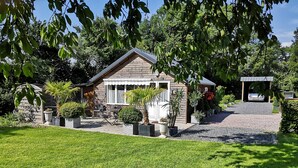 Une maison en bois avec un porche, entourée d’une pelouse bien entretenue et agrémentée de diverses plantes en pot.