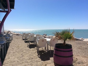 Ristorante sulla spiaggia con posti a sedere all'aperto, una pianta di palma e vista sul mare.