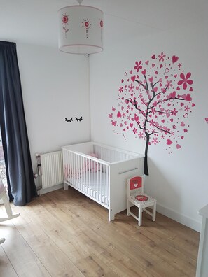 Un berceau blanc orné d’un autocollant représentant un arbre rose sur le mur, une petite chaise et un radiateur.