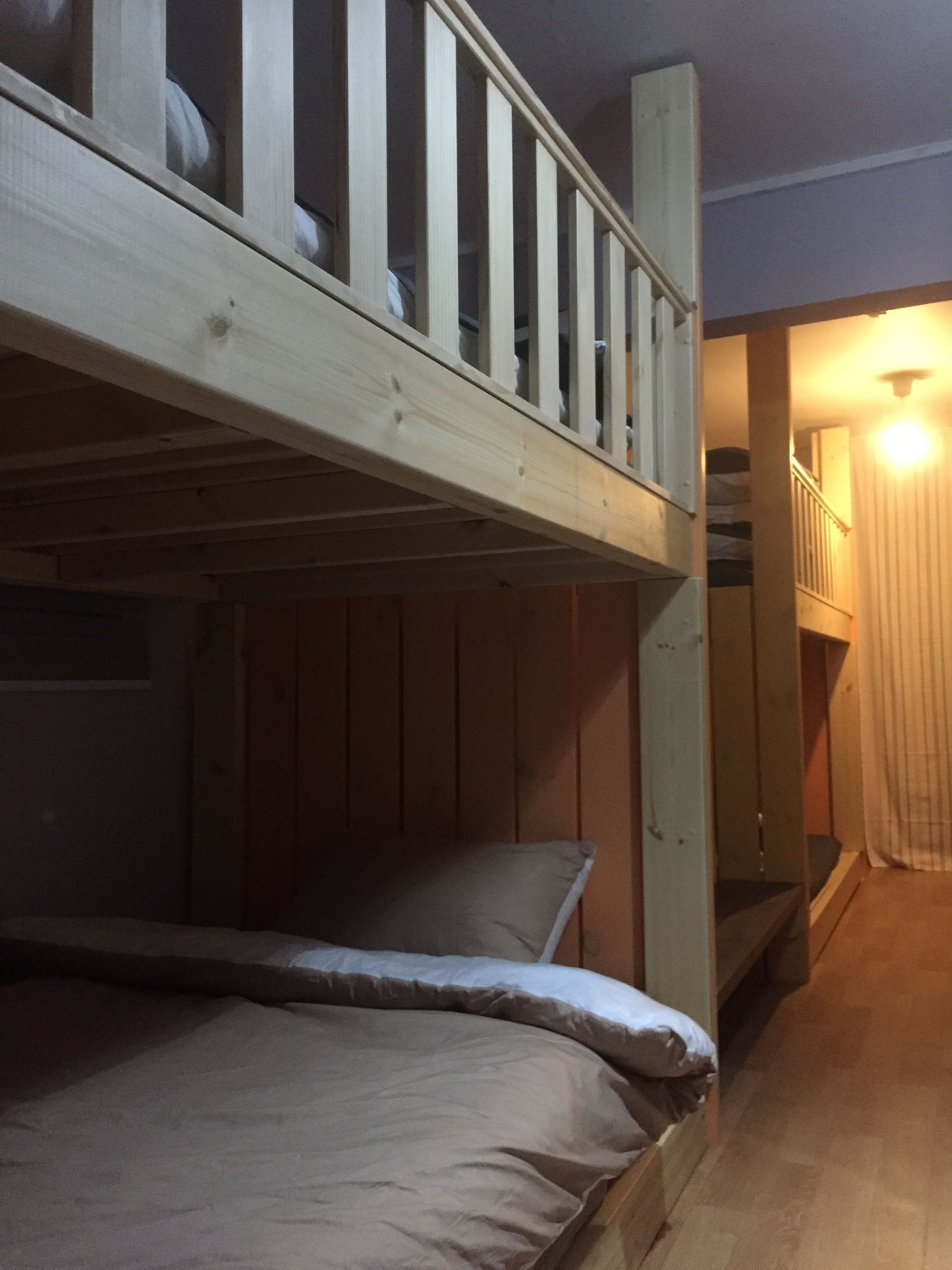 A bunk bed room with a wooden headboard, a staircase leading to an upper level, and a lit hallway.