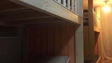 A bunk bed room with a wooden headboard, a staircase leading to an upper level, and a lit hallway.
