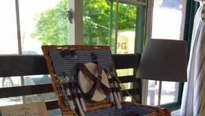A wicker picnic basket with a checkered cloth inside, placed on a table with a plaid tablecloth. A book titled 'Year of Picnics' is visible on the table.
