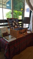 Una cesta de mimbre para picnic con un forro a cuadros, sobre una mesa con mantel escocés. Se ve un libro titulado 'Year of Picnics' sobre la mesa.