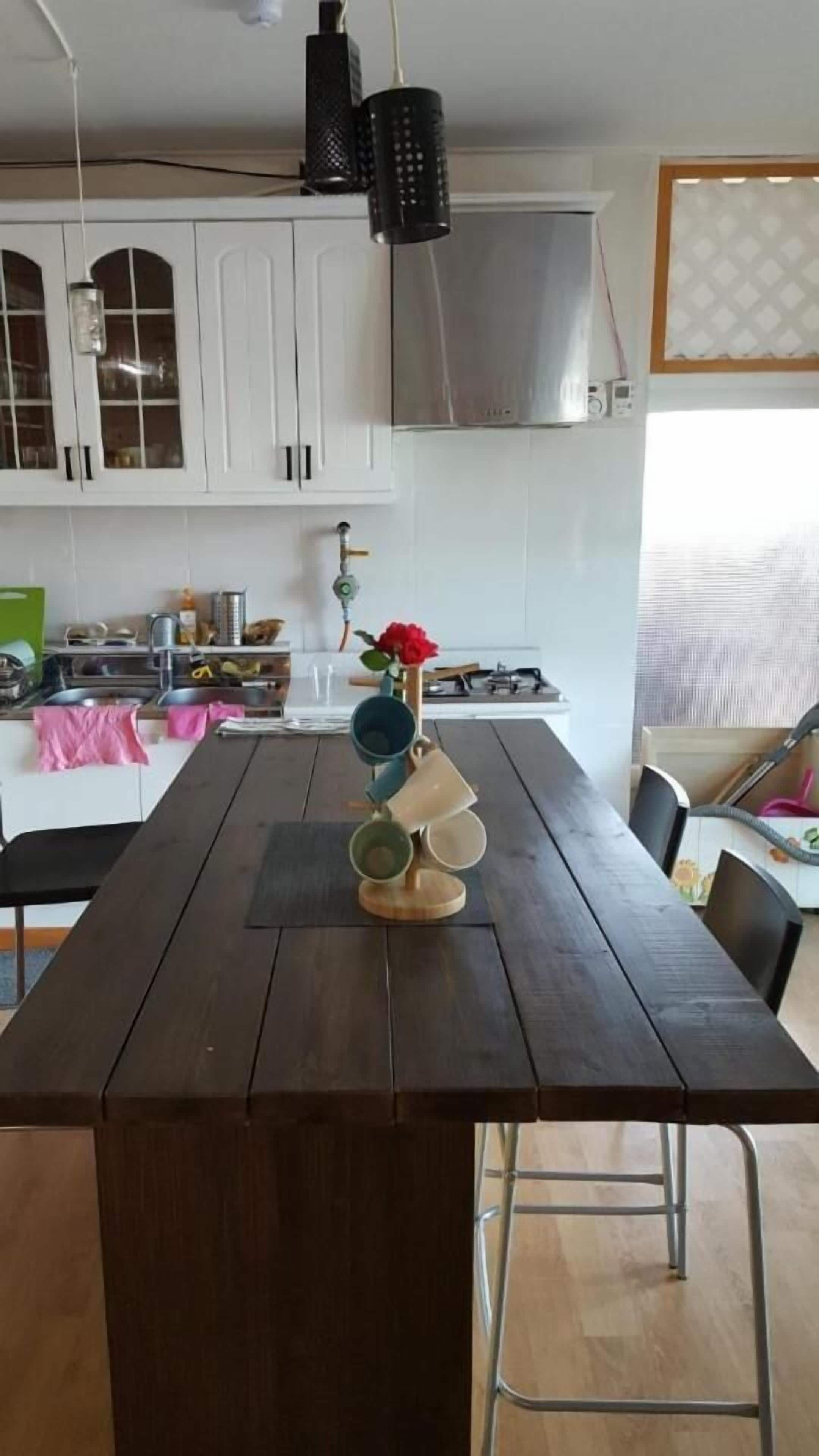 Cozinha com armários brancos, exaustor de aço inoxidável e mesa de jantar de madeira com cadeiras.