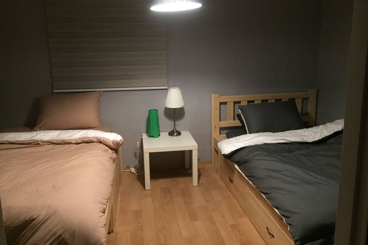 A small, dimly lit room with two beds, a nightstand, and a lamp.