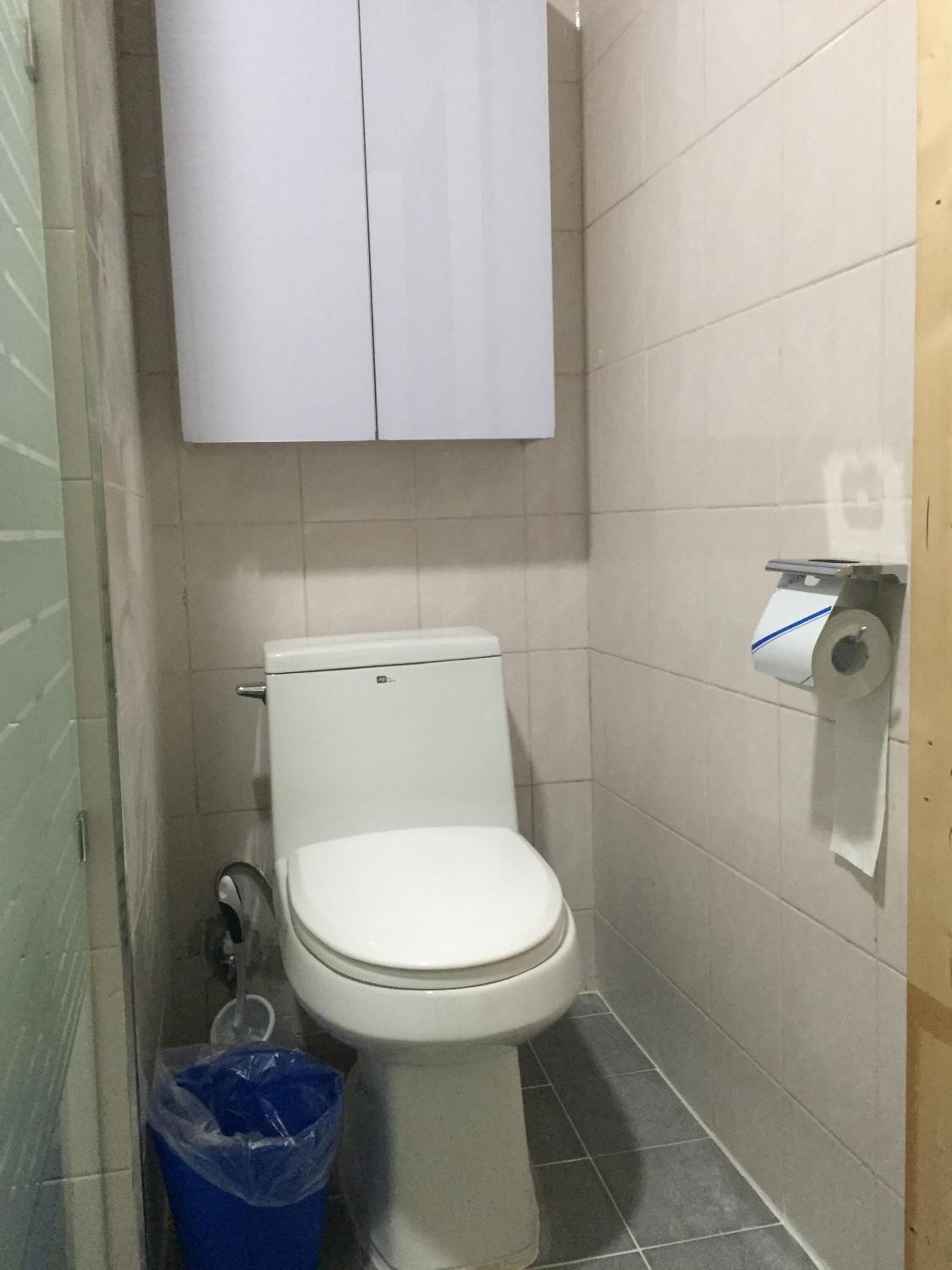 Un baño pequeño con inodoro, dispensador de toallas de papel y un cubo de basura azul.