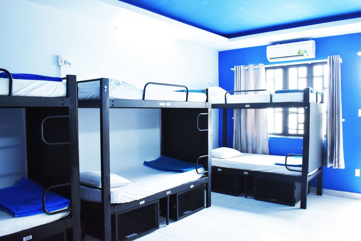 Quarto com beliches, janela com cortinas e ar condicionado na parede.