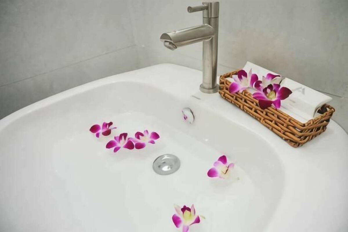 Une baignoire blanche avec un robinet argenté, un panier en osier contenant un linge blanc et des pétales de fleurs roses sur le bord.