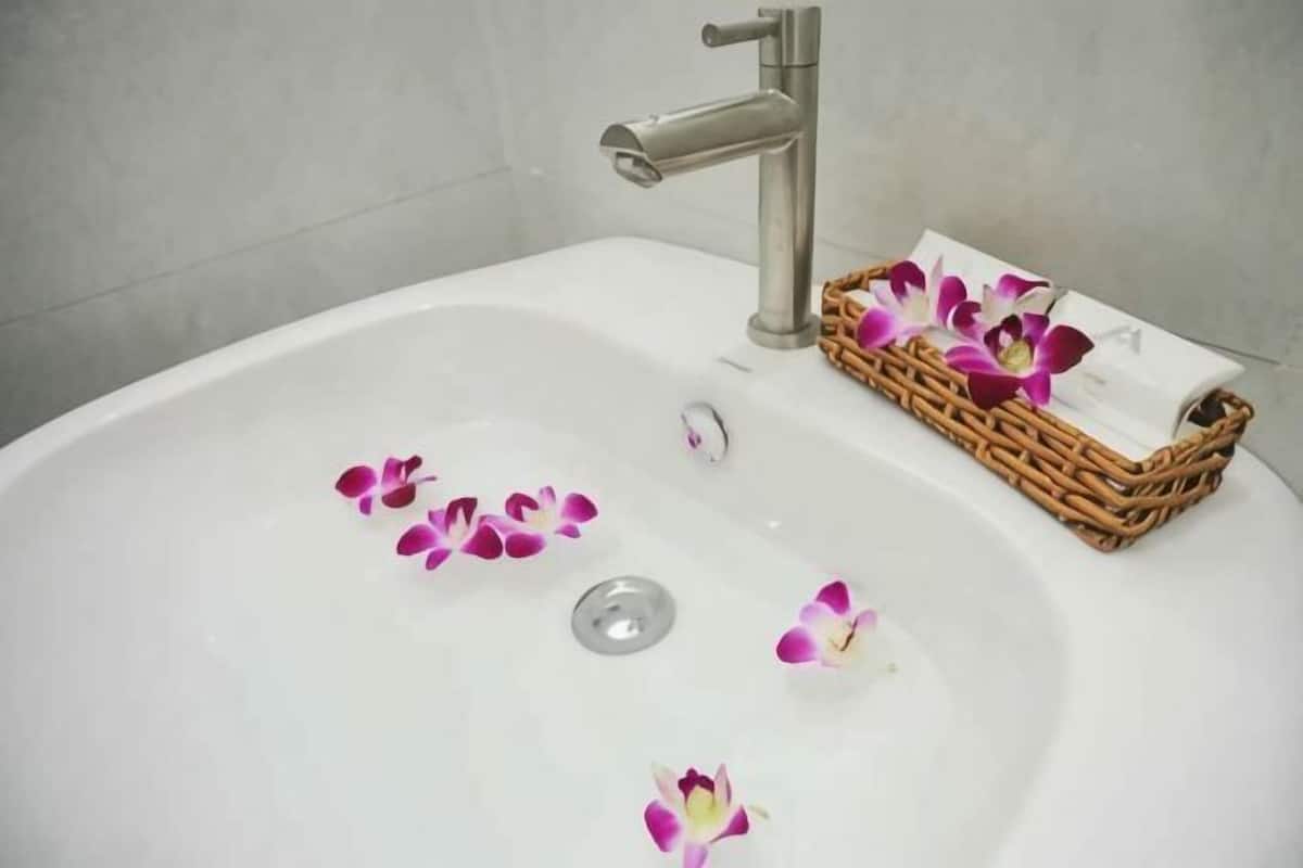 Una banyera blanca amb un faucet platejat, una cistella de vimet amb drap blanc i pètals de flors roses a la superfície.
