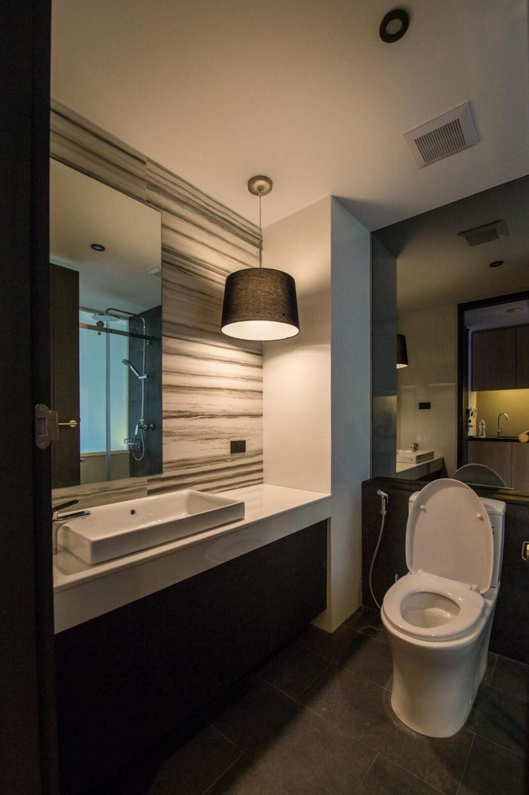 Een moderne badkamer met een grote spiegel, een witte wastafel, een toilet en een hangende hanglamp.